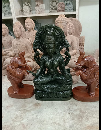 Masterful green stone carving featuring a warrior goddess with weapons and protective stance